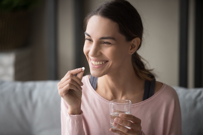 Woman smiling at a pill with a glass of water in her hand