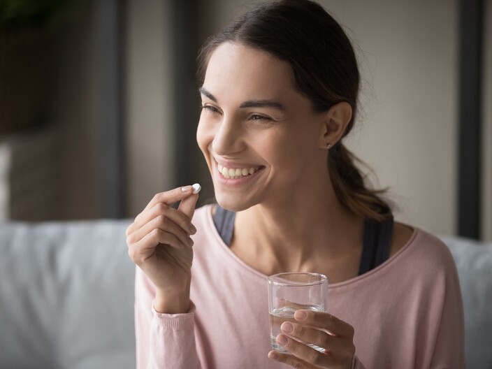 Woman smiling at a pill with a glass of water in her hand