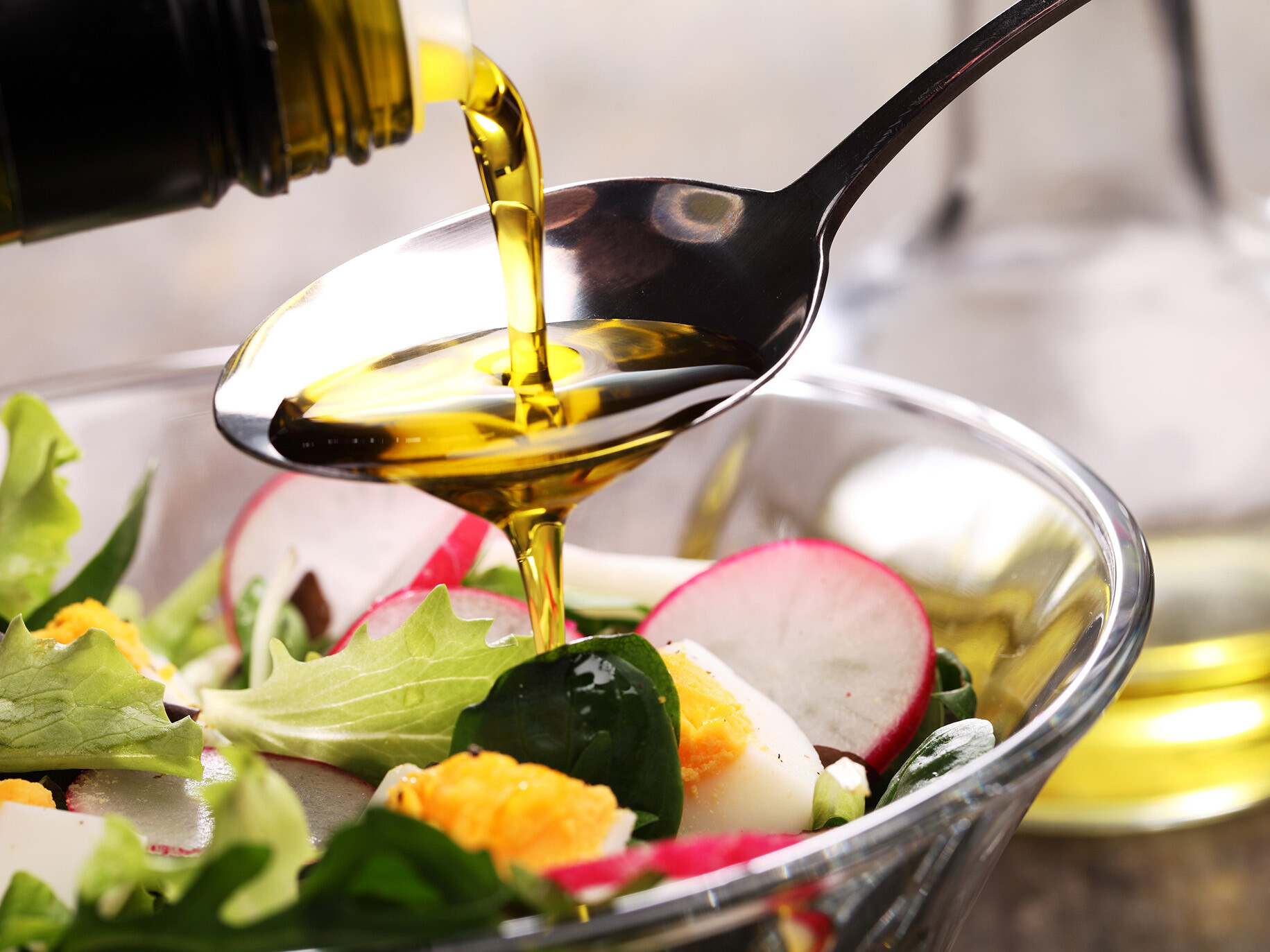 Oil pouring on a spoon over a bowl of salad